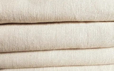 A stack of folded, natural-colored linen fabric. This image showcases the texture of linen, confirming that is linen a natural fiber.