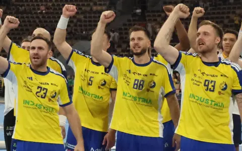 Piłkarze ręczni świętują zwycięstwo w Lidze Mistrzów. Drużyna w żółtych koszulkach z numerami 23, 5, 88 i 93 wznosi ręce w geście triumfu.