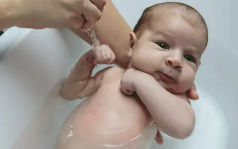 Niemowlę w wannie, delikatnie kąpane. Widoczny wypukły pępek maluszka.