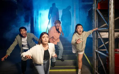 Grupa przerażonych ludzi ucieka przed postaciami w dymie. To wygląda jak prawdziwy escape room, gdzie trzeba rozwiązać zagadki, by przeżyć.
