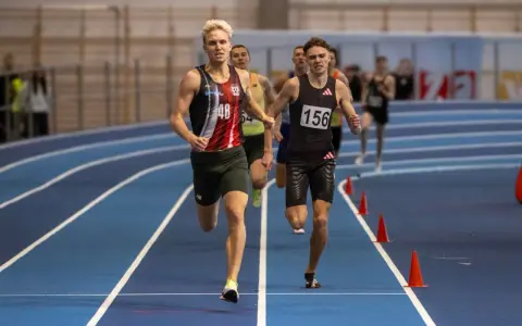 Filip Ostrowski biegnie w zawodach lekkoatletycznych. Dwóch zawodników na pierwszym planie, jeden z numerem 48, drugi z 156.