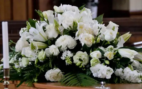 Un arreglo floral blanco sobre un ataúd, con lirios, rosas y otras flores. Estas flores para difuntos simbolizan paz y pureza en el adiós.