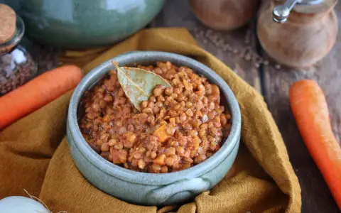 Un invitante ragù di lenticchie, profumato con alloro, pronto per essere gustato. Accanto, carote fresche e cipolla.