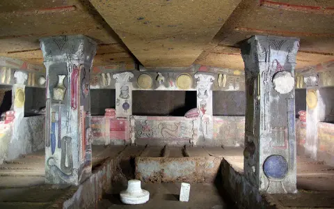 Inside a tomb at the Cerveteri Necropolis, painted columns and walls depict ancient life.