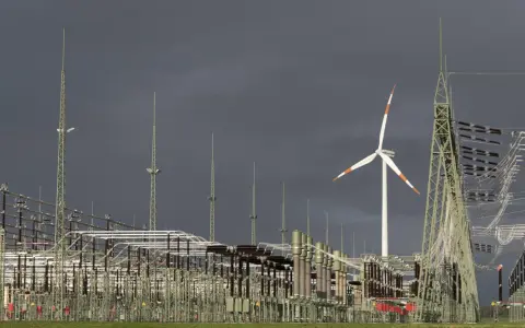 Ein Windrad und eine weitläufige Schaltanlage symbolisieren den Ausbau des Stromnetzes für erneuerbare Energien.