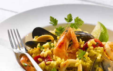 Pyszne risotto z owocami morza: krewetki, małże, kalmary i ryż, udekorowane natką pietruszki i ćwiartką limonki.