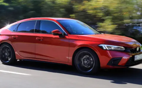 Czerwony Honda Civic 2025 pędzi po drodze, otoczony rozmazaną zielenią drzew.