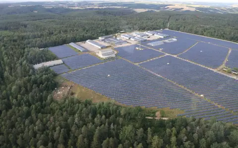 Große Solaranlage im Wald, die Sonnenenergie sammelt. Gebäude und Reihen von Solarmodulen erstrecken sich über die Landschaft.