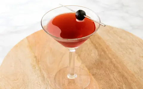 Czerwony drink w kieliszku koktajlowym, ozdobiony oliwką na wykałaczce. Idealny drink San Francisco na letnie wieczory.