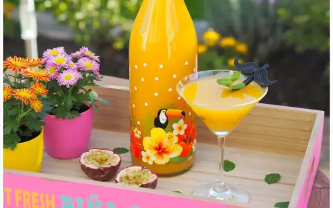 Tropische Früchte und ein leuchtend gelber Drink auf einer rosa Holzschale. Ein ideales Solero Schnaps Rezept ohne Sahne für heiße Tage.