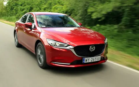 Czerwona Mazda 6 2.0 benzyna pędzi po wiejskiej drodze, otoczona zielenią drzew.