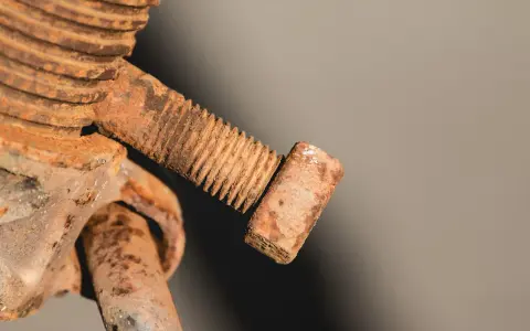Zapieczona śruba, pokryta grubą warstwą rdzy, wygląda jak relikt przeszłości. Jej gwint jest ledwo widoczny pod brązowym nalotem.
