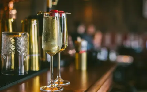Dwa kieliszki musującego drinku z Prosecco i Cava, ozdobione malinami, stoją na barze obok stylowych akcesoriów.