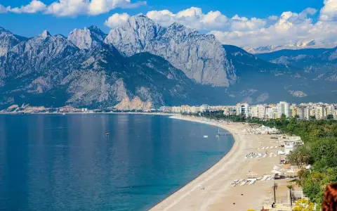 Ein malerischer antalya strand mit türkisfarbenem Wasser, weißen Bergen im Hintergrund und einer Stadtkulisse.
