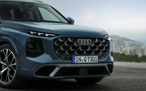 Przód eleganckiego Audi Q7 3.0 TDI w kolorze granatowym, z charakterystycznym grillem i światłami LED, na tle miejskiego krajobrazu.