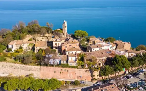 Borgo antico con campanile affacciato sul mare Adriatico. Il centro storico del lungomare Gabicce Mare, con tetti rossi e vegetazione rigogliosa, si estende verso l'azzurro intenso dell'acqua.