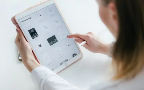 Kobieta tworzy rysowanie na iPadzie, przeglądając swoje prace. Stylus w dłoni sugeruje cyfrowe tworzenie.