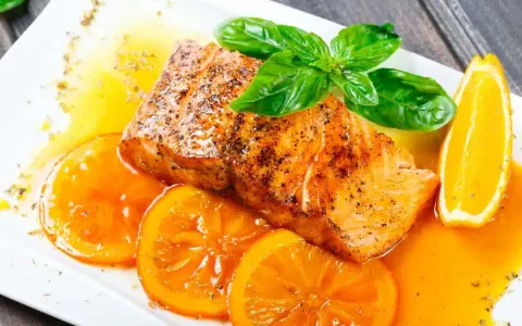 Delicioso salmón a la naranja, servido con rodajas de naranja fresca y hojas de albahaca.