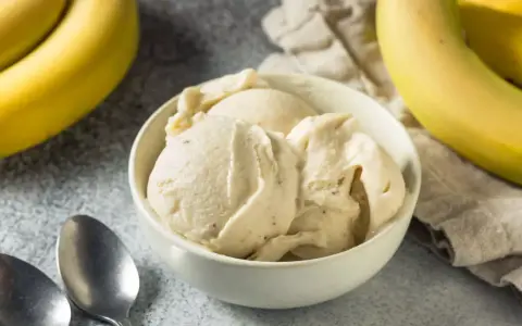 Un cremoso helado de plátano en un tazón blanco, con plátanos amarillos frescos al lado.