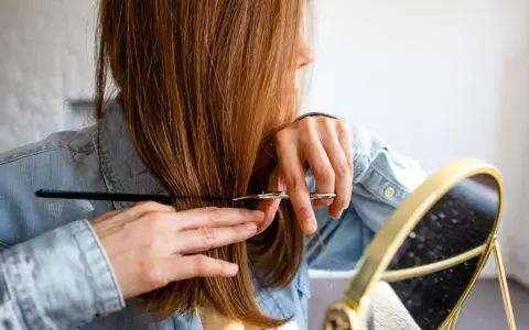 Frau mit langen, braunen Haaren, die sich im Spiegel die Haare schneidet.