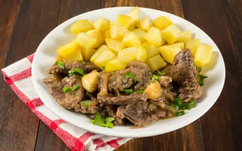 Plato de higaditos de pollo en salsa con patatas fritas en cubos, decorado con perejil fresco.