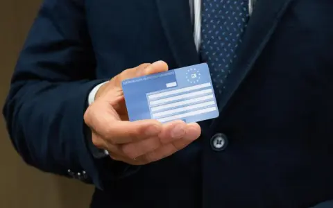 Dłoń trzyma Europejską Kartę Ubezpieczenia Zdrowotnego. Czy EKUZ działa w UK? Tak, karta zapewnia dostęp do opieki medycznej w Wielkiej Brytanii.