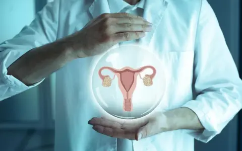 Dłonie lekarza w białym fartuchu trzymają bańkę z grafiką narządów rodnych kobiety.