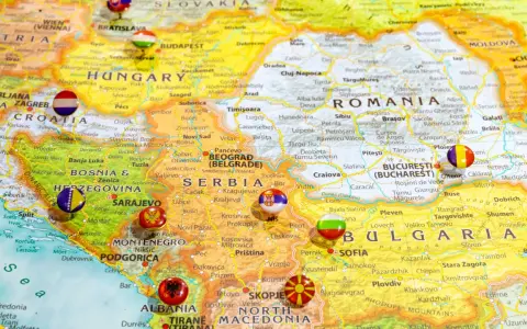Mapa Europy z zaznaczonymi krajami bałkańskimi, w tym Serbią, Bułgarią i Rumunią, z flagami narodowymi w miejscach stolic.