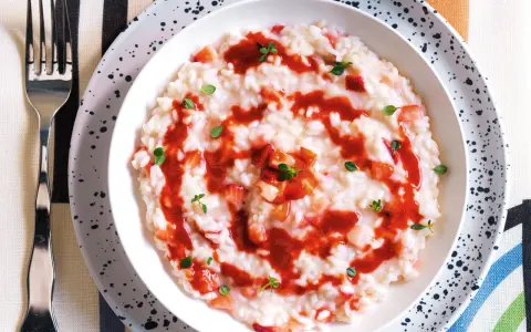 Un cremoso risotto alle fragole, guarnito con salsa di fragole e foglioline verdi, pronto per essere gustato.