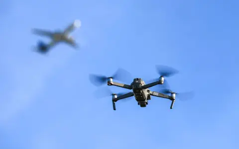Ein moderner Drohne fliegt im Vordergrund, im Hintergrund ein unscharfes Flugzeug.