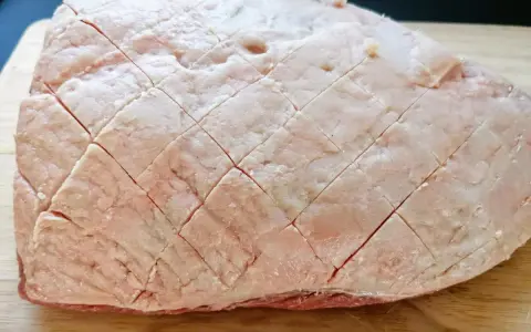 Un pezzo di picanha alla griglia, con la sua copertura di grasso incisa a rombi, pronto per essere cotto su un tagliere di legno.