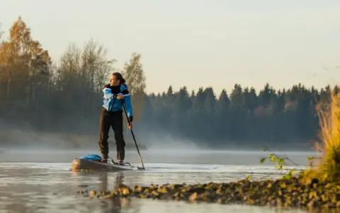 Mann auf Stand Up Paddle, achtet auf die ruhige Wasseroberfläche und die neblige Morgenstimmung.