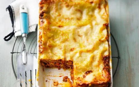 Eine frisch gebackene, italienische Lasagne in einer Auflaufform, mit einer goldbraunen Käseschicht und einem Stück herausgenommen.