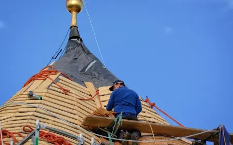 Dekarz na dachu pracuje nad pokryciem, zastanawiając się, ile zarabia dekarz w Niemczech.