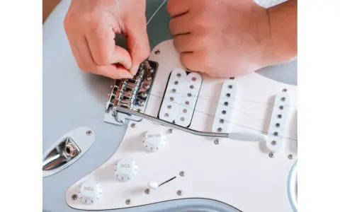 Ręce montują struny do mostka gitary elektrycznej. To ważny krok, jak zrobić gitarę elektryczną, by brzmiała idealnie.