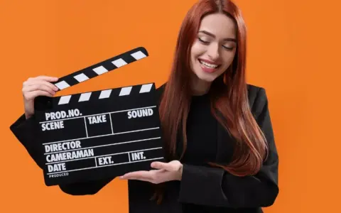 Uśmiechnięta kobieta z rudymi włosami trzyma klaps filmowy. Zastanawiasz się, ile kosztuje hollywood smile w Polsce?