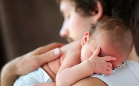 Padre abbraccia neonato. Osservare attentamente i sintomi autismo nel neonato di 3 mesi, come la mancanza di contatto visivo o risposte emotive atipiche.
