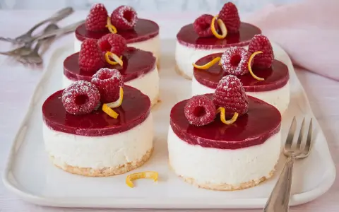 Sechs kleine Kuchen mit Himbeeren und Zitronenzesten auf einem weißen Teller.