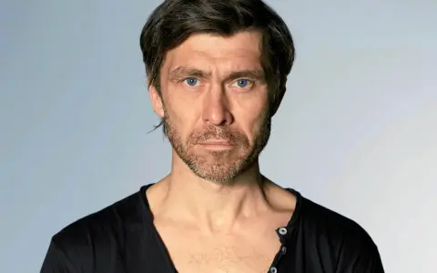 Marcin Czarnik, aktor o intensywnym spojrzeniu i niebieskich oczach, w czarnej koszulce.