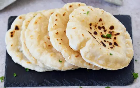 Frisch gebackenes pita brot, leicht gebräunt und mit Petersilie garniert, liegt auf einem dunklen Stein.