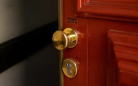 Poignée et serrure dorées sur une porte rouge. Une étiquette indique un service de serrurerie, utile en cas de porte forcée, pour l'assurance propriétaire ou locataire.