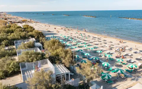Lidi ferraresi: una distesa di ombrelloni verdi e bianchi sulla sabbia dorata, con il mare azzurro e alcune persone che si godono il sole.