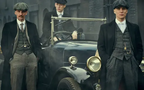 Tre uomini in abiti eleganti, stile Peaky Blinders, posano accanto a un'auto d'epoca.
