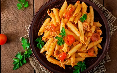 Penne z kurczakiem i pomidorami, udekorowane natką pietruszki. Idealne pytanie: co dzisiaj ugotować na obiad?
