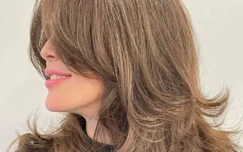 Mujer sonríe con un corte mariposa pelo largo, con capas que enmarcan su rostro.