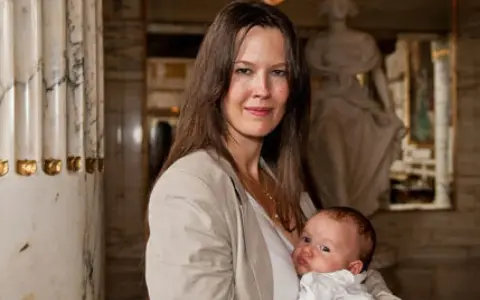 Elin Klinga med sitt barn. En vacker mamma med sitt nyfödda barn i famnen, omgivna av klassisk arkitektur.