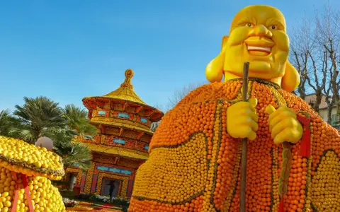 Escultura gigante de Buda hecha de naranjas y limones, parte del menton lemon festival, con una pagoda de frutas al fondo.