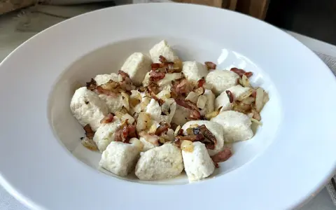 Pyszna keto kolacja z twarogiem w formie kluseczek, posypana chrupiącym boczkiem i cebulką.