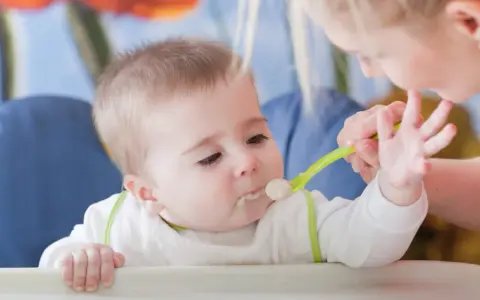 Mama karmi dziecko pierwszą łyżeczką do karmienia. Maluch z zaciekawieniem patrzy na jedzenie.