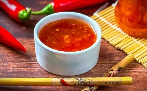 Schüssel mit leuchtend roter Sweet Chilli Sauce, daneben rote Chilis und Stäbchen. Perfekt für dein Sweet Chilli Sauce Rezept!